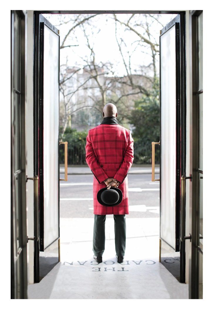 A doorman in a red greatcoat framed in an open doorway